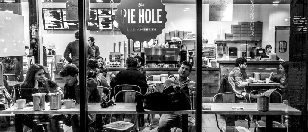 Black and white picture, looking through the glass at customers in Pie Hole Restaurant.