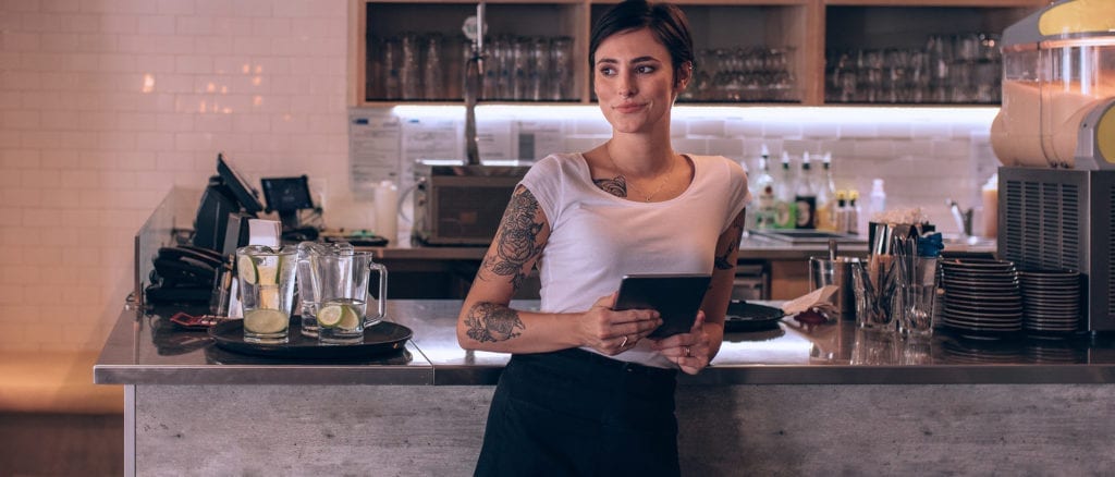 Female store owner in front of counter holding tablet.