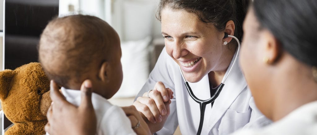 Smiling nurse looking at baby holding teddy bear